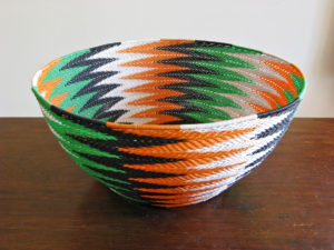 Side-on view of the completed Animals Asia basket in black, white, orange and green telephone wires in a chevron pattern