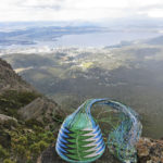 Blue, black, green and white telephone-wire basket in its mould. On rocks on Mt Wellington, with Hobart and the Derwent Estuary in the distance.