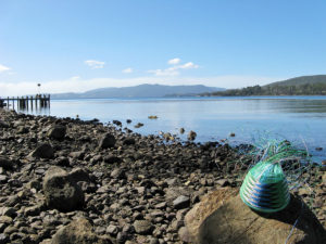 Telephone wire basket on the rocky beach at Lunnawunna, Bruny Island, Tasmania, with the jetty in the background.