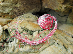 Red and white wire basket in progress, nestled on a weathered sandstone rock face.