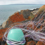 Wire basket in progress on a tupperware mould, on lichen-covered rocks on Kangaroo Island, with the sea and the Australian mainland in the background.