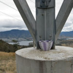 Purple, white and black wire basket resting on a concrete pylon on Mt direction, with the River Derwent, Hobart northern suburbs and the Mt Wellington range in the background.