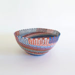 Side view of a large, handwoven telephone wire basket in a striking pattern of orange, blue and white wires.