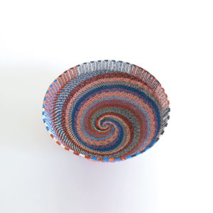 View of the spiralling inside base of a large, handwoven telephone wire basket in a striking pattern of orange, blue and white wires.