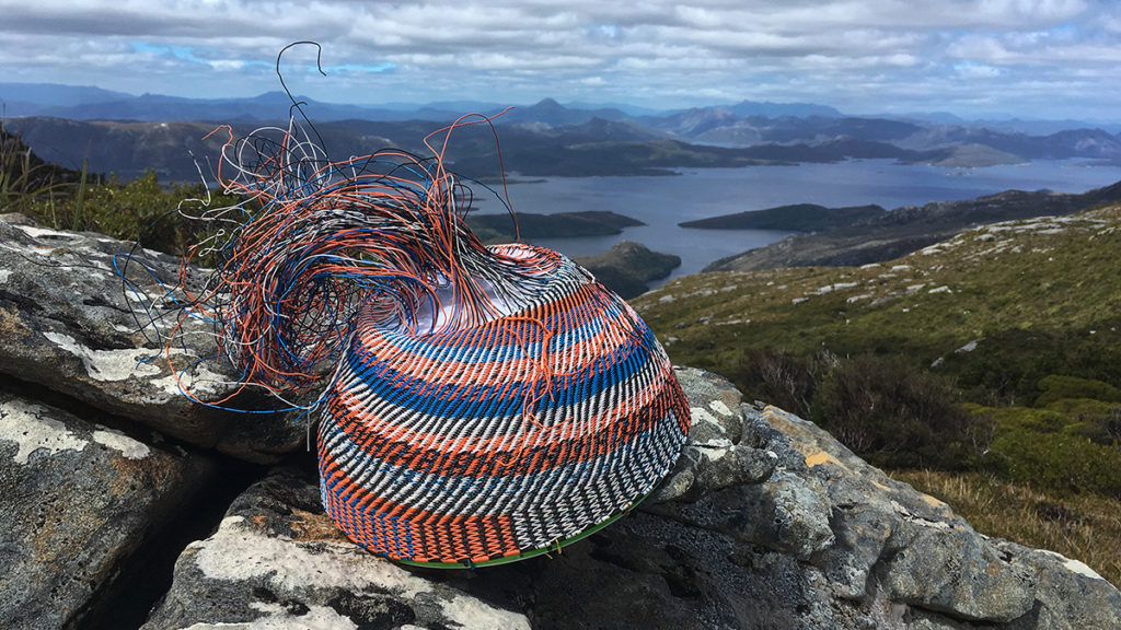 A wire basket in progress on a large boulder with the Lake Pedder impoundment in the distance.